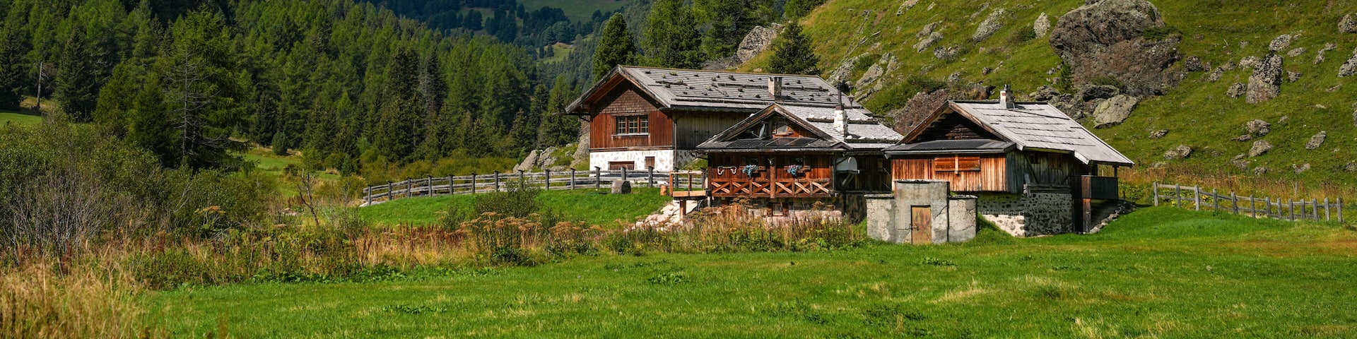 A mountain landscape with a wooden house, green fields, and rocky peaks.