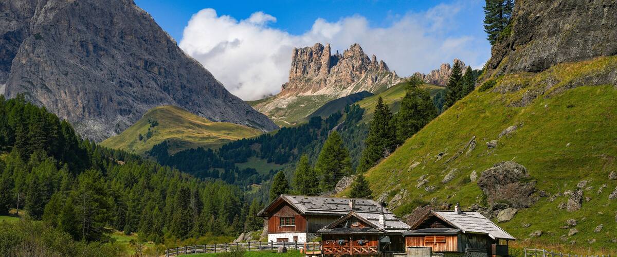 A mountain landscape with a wooden house, green fields, and rocky peaks.