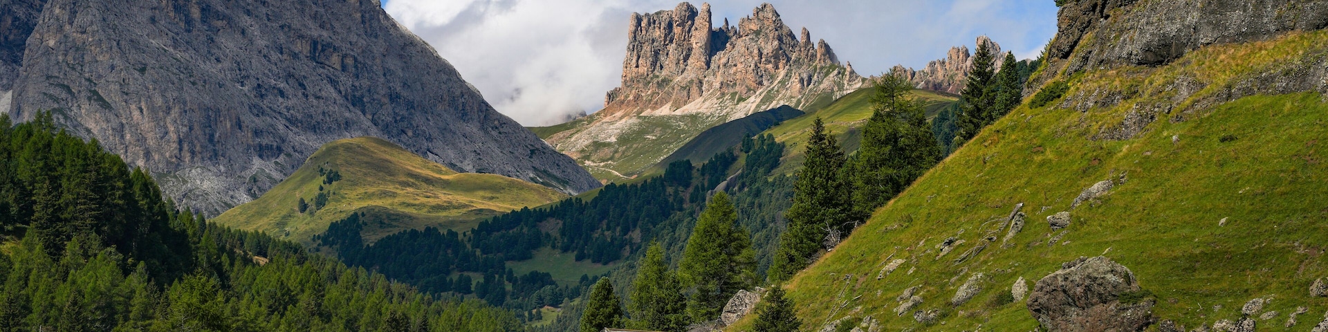 A mountain landscape with a wooden house, green fields, and rocky peaks.