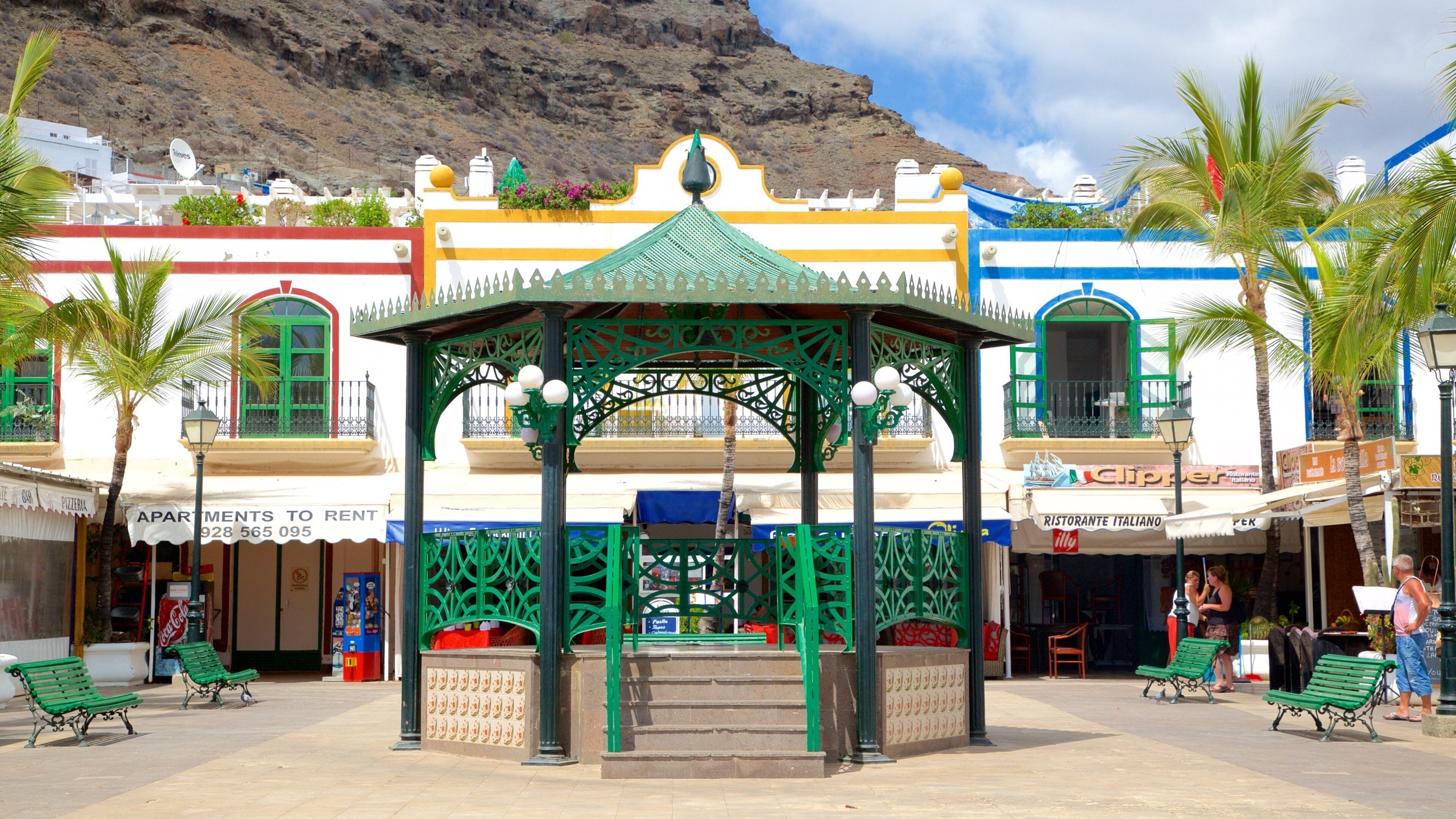 Una plaza con un quiosco verde, palmeras y edificios coloridos.