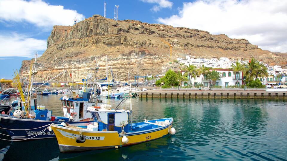 A harbor with boats, a lighthouse, and a rocky hill with buildings.