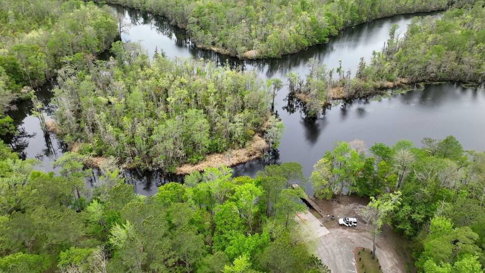 A river winding through a dense forest with a small dock and a white truck parked nearby.
