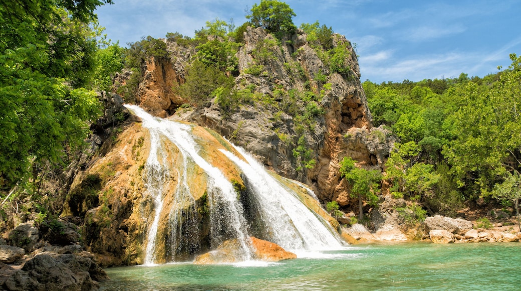 A waterfall cascading into a turquoise pool surrounded by rocky cliffs and lush greenery.