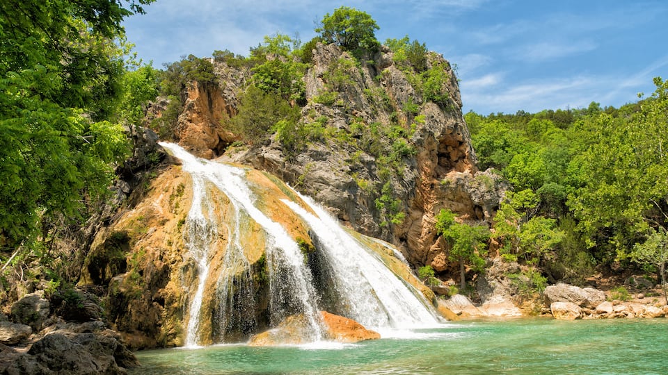 A waterfall cascading into a turquoise pool surrounded by rocky cliffs and lush greenery.