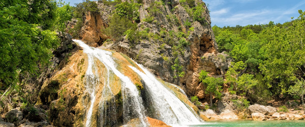 A waterfall cascading into a turquoise pool surrounded by rocky cliffs and lush greenery.