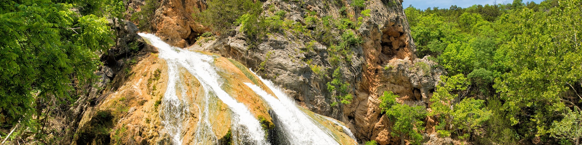 A waterfall cascading into a turquoise pool surrounded by rocky cliffs and lush greenery.