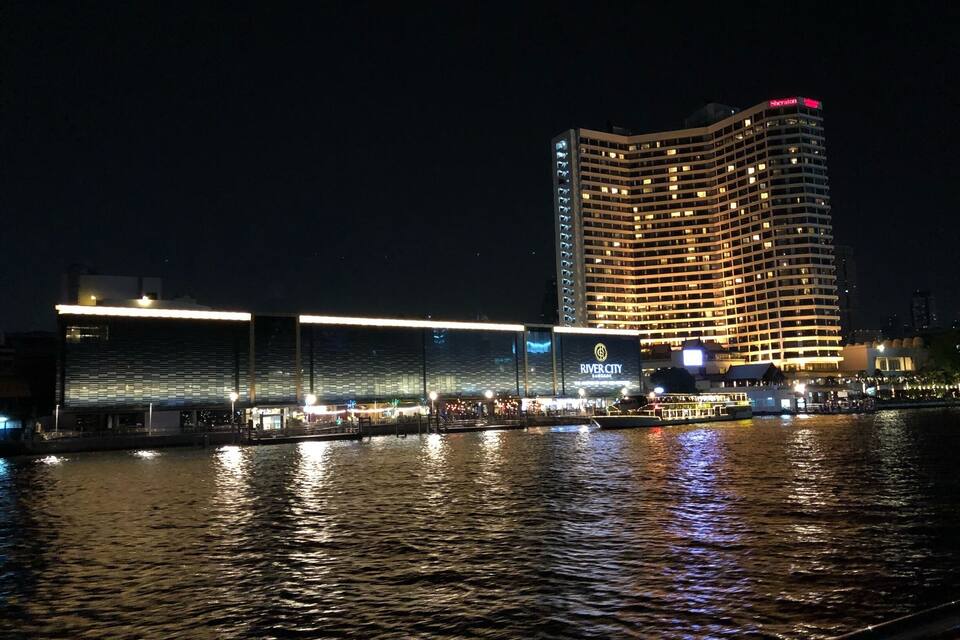 Un hôtel situé au bord de l’eau, avec des fenêtres illuminées et une rivière au premier plan.