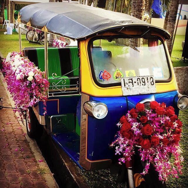 Un tuk-tuk colorido adornado con flores estacionado en un camino adoquinado.