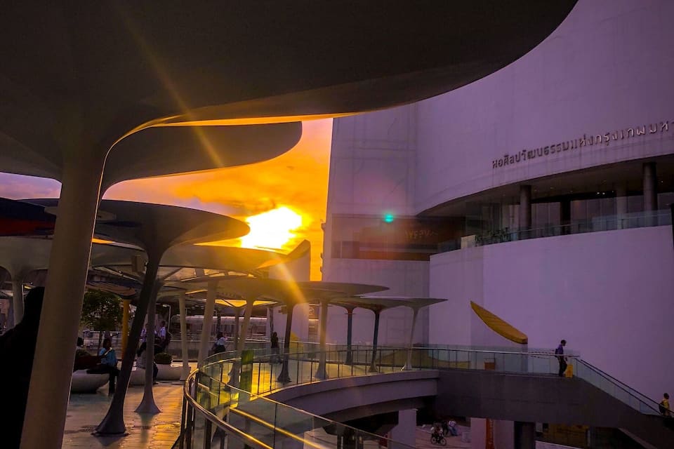 An outdoor area with a modern building, a glass railing, and a sunset in the background.