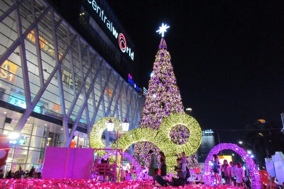 A large illuminated Christmas tree with a star on top in front of a shopping mall.