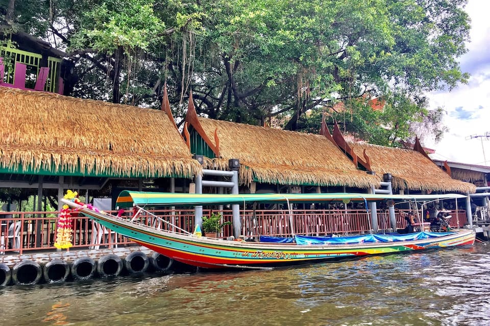 A colorful boat docked at a pier with thatched-roof buildings in the background.