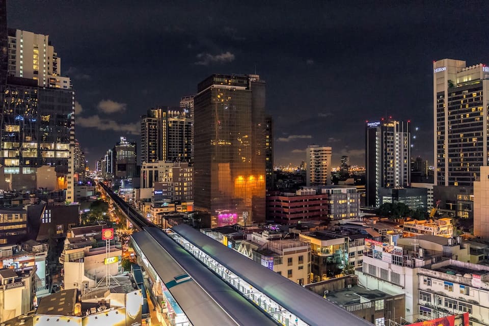 A nighttime cityscape with a prominent train track running through the center, surrounded by high-rise buildings and illuminated signs.