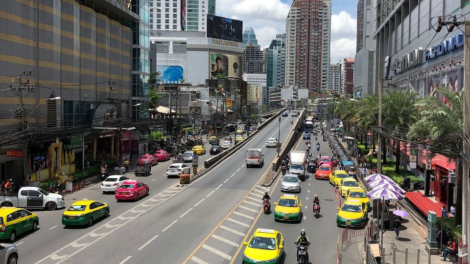 A busy urban street with tall buildings, including a hotel and a shopping mall.