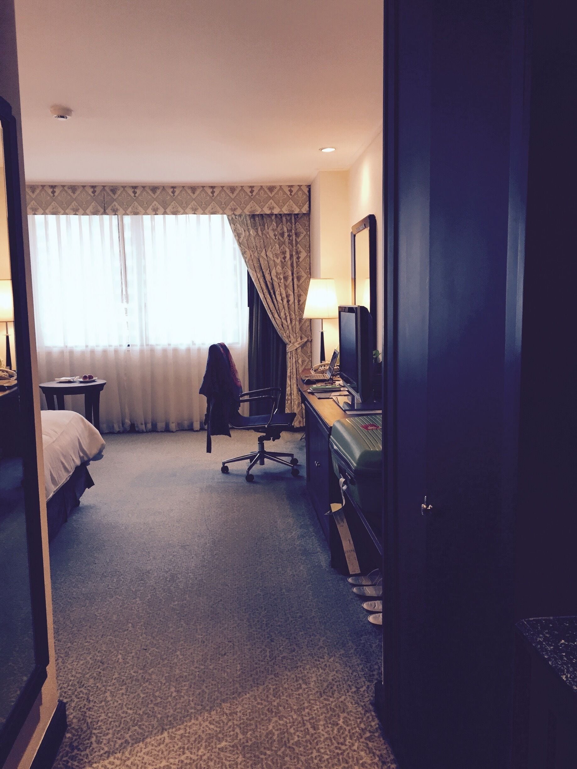 Quarto de hotel com cama, escrivaninha, cadeira e um espelho grande.