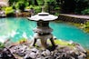 Un farol de piedra junto a un estanque turquesa rodeado de rocas y follaje.