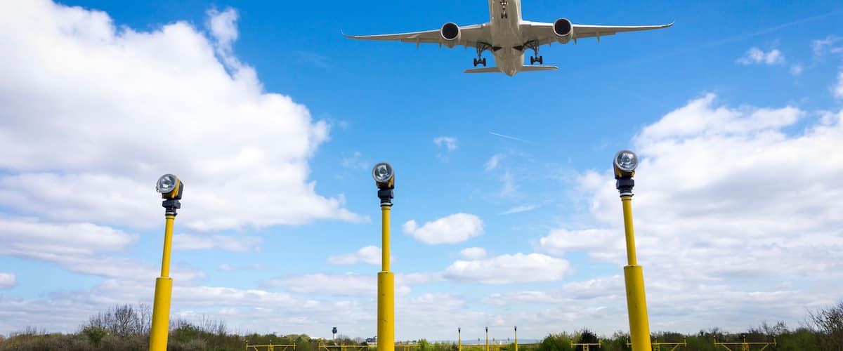 Ein Flugzeug fliegt über eine Landschaft mit gelben Pfosten und blauem Himmel.