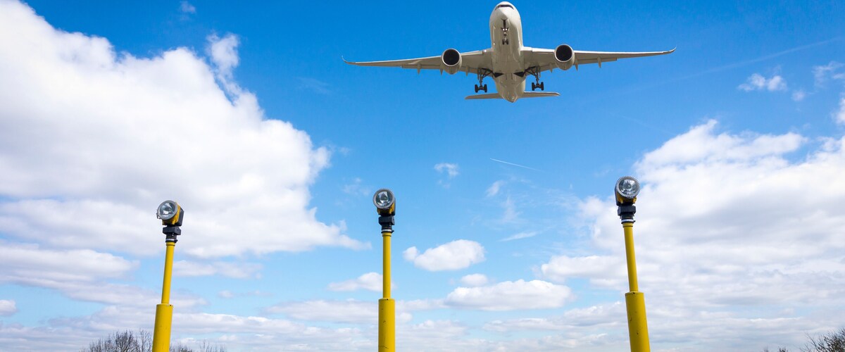 An airplane flying over a landscape with yellow poles and a clear blue sky.