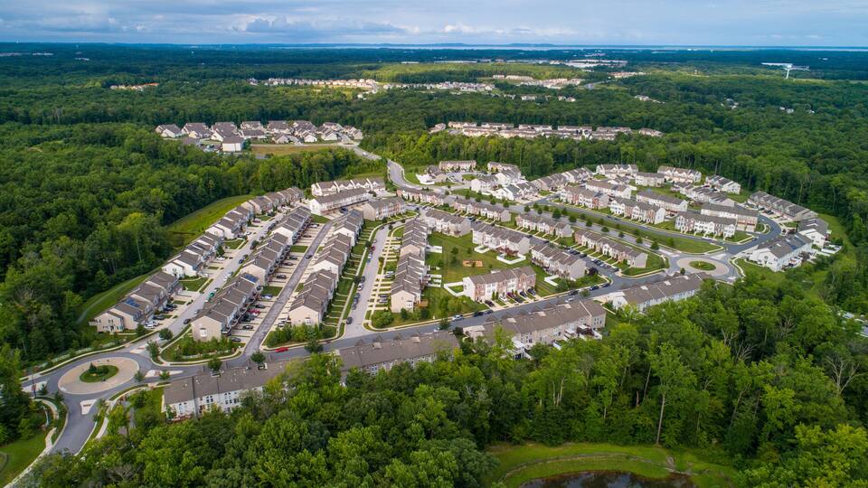 A residential area with houses arranged in a circular pattern, surrounded by dense forests and a lake.