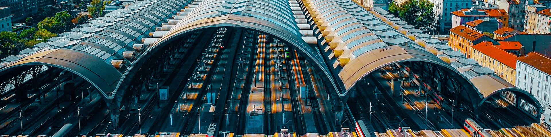 Aerial view of the station where trains arrive. An old arched structure made of metal and glass above the station poles. Tourism. Transport. Skyline with tall buildings. Italy, Milan, 09.2022
