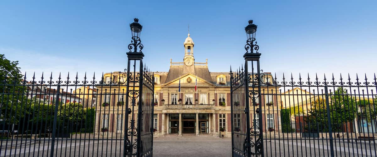 A historic building with a clock tower, ornate iron gates, and a cobblestone entrance.