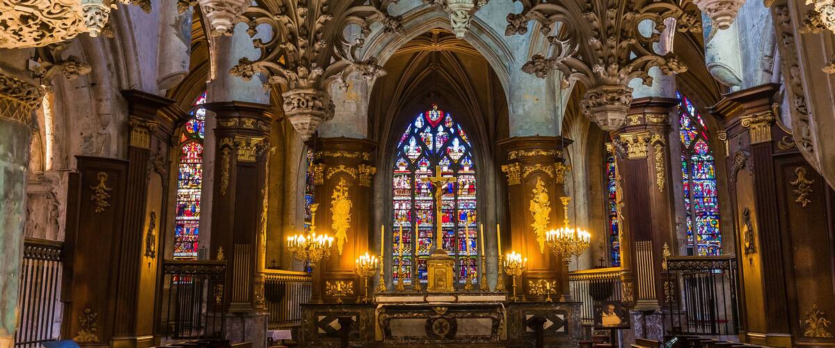 An ornate Gothic church interior with intricate stone carvings, stained glass windows, and a central altar.