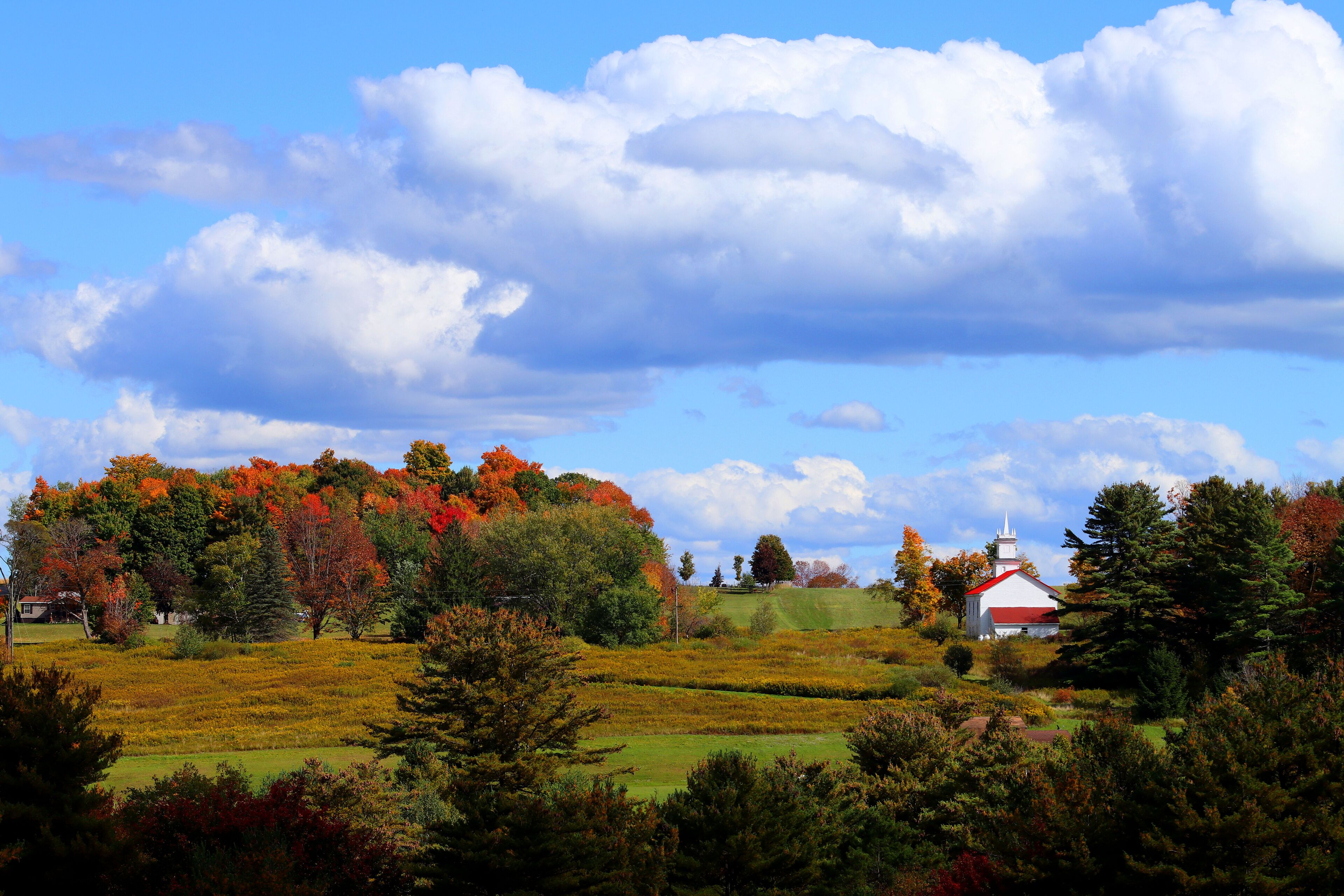 A rural landscape with a white church, autumn-colored trees, and a clear blue sky.