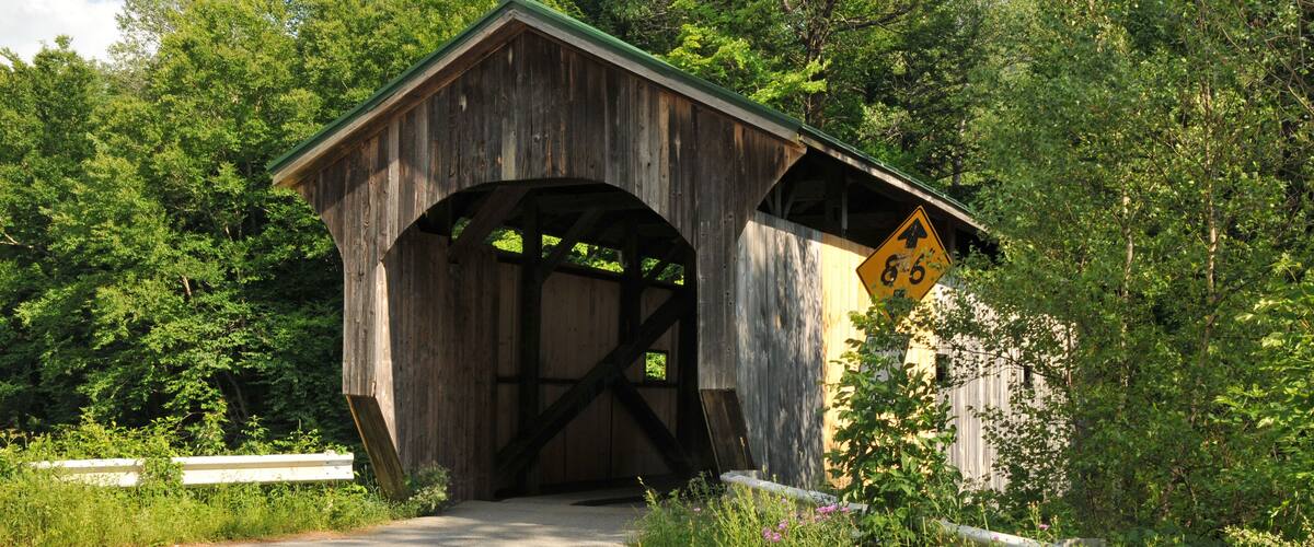 A wooden covered bridge with a '4-6-8' sign, surrounded by lush greenery and trees.