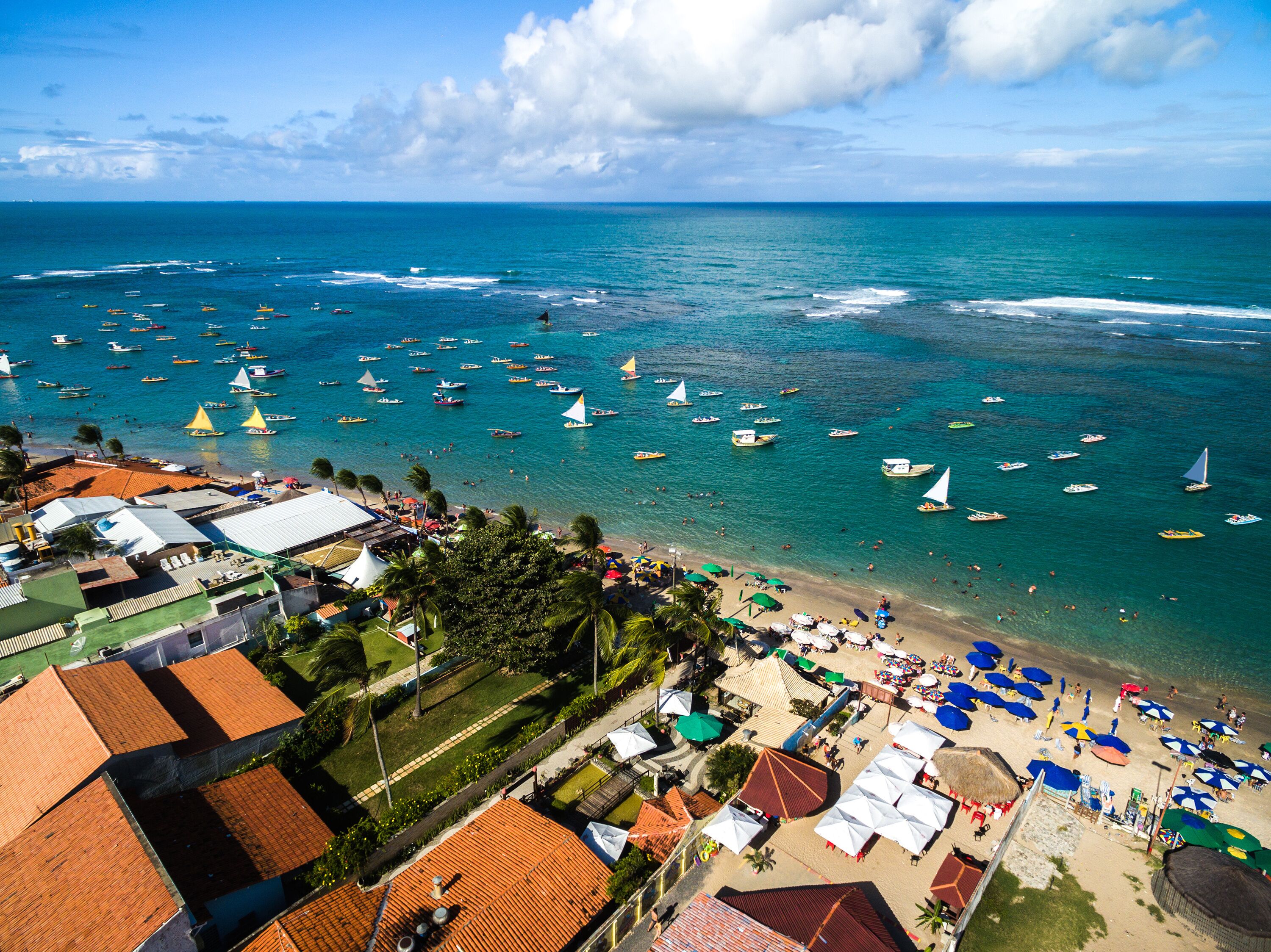 A coastal town with a beach, boats, and buildings with red-tiled roofs.