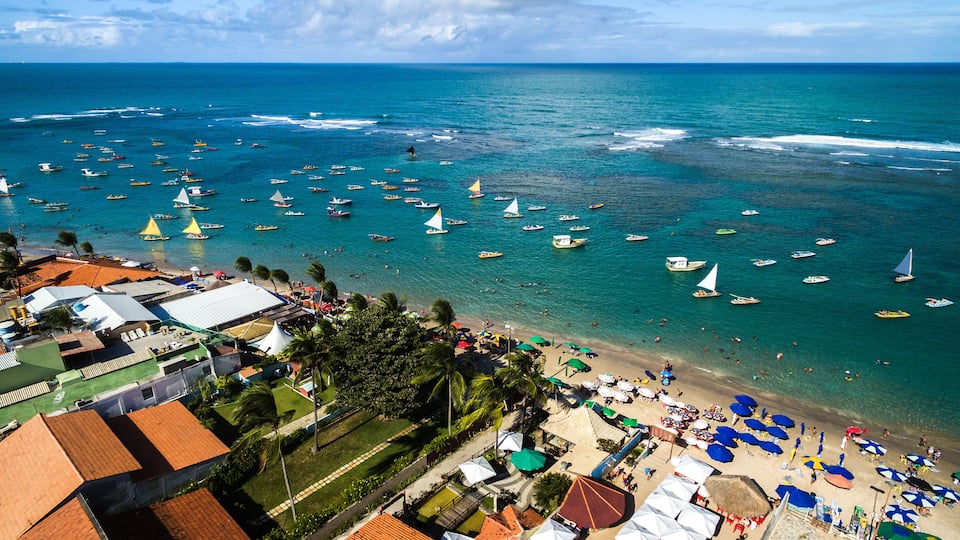 A coastal town with a beach, boats, and buildings with red-tiled roofs.