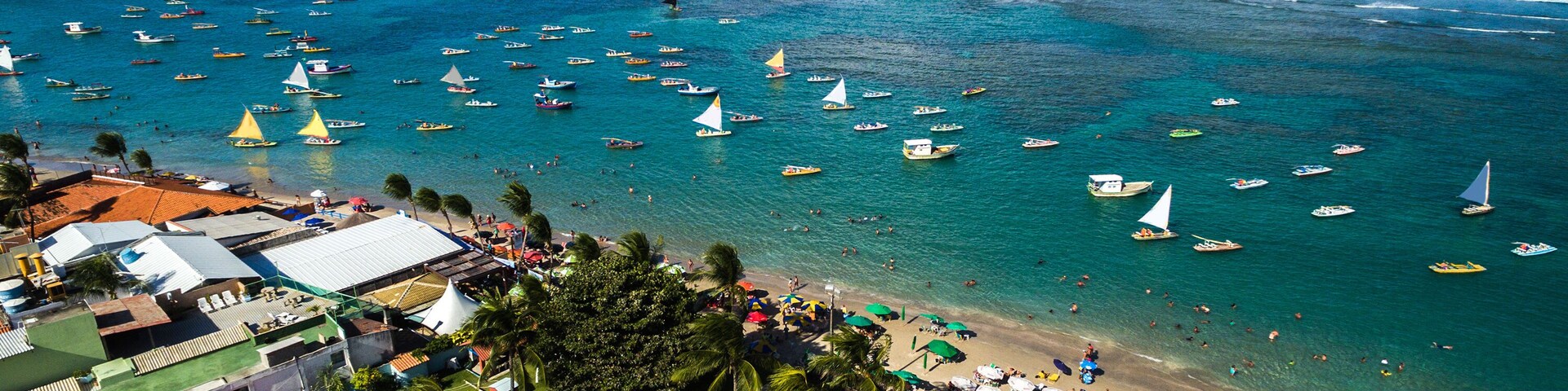 Uma vila costeira com praia, barcos e edifícios com telhados vermelhos.
