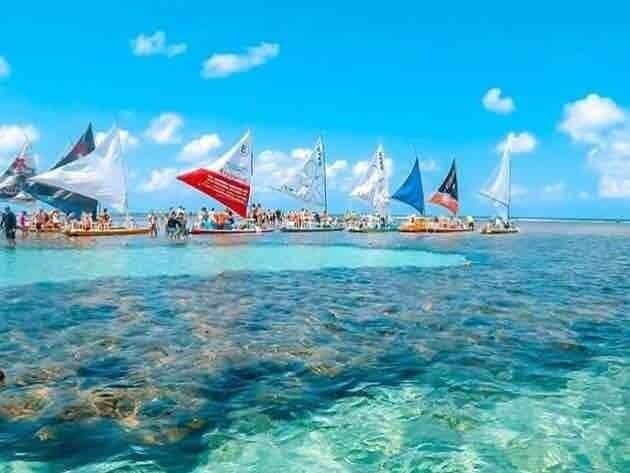 A clear blue sea with several sailboats with colorful flags anchored near the shore.