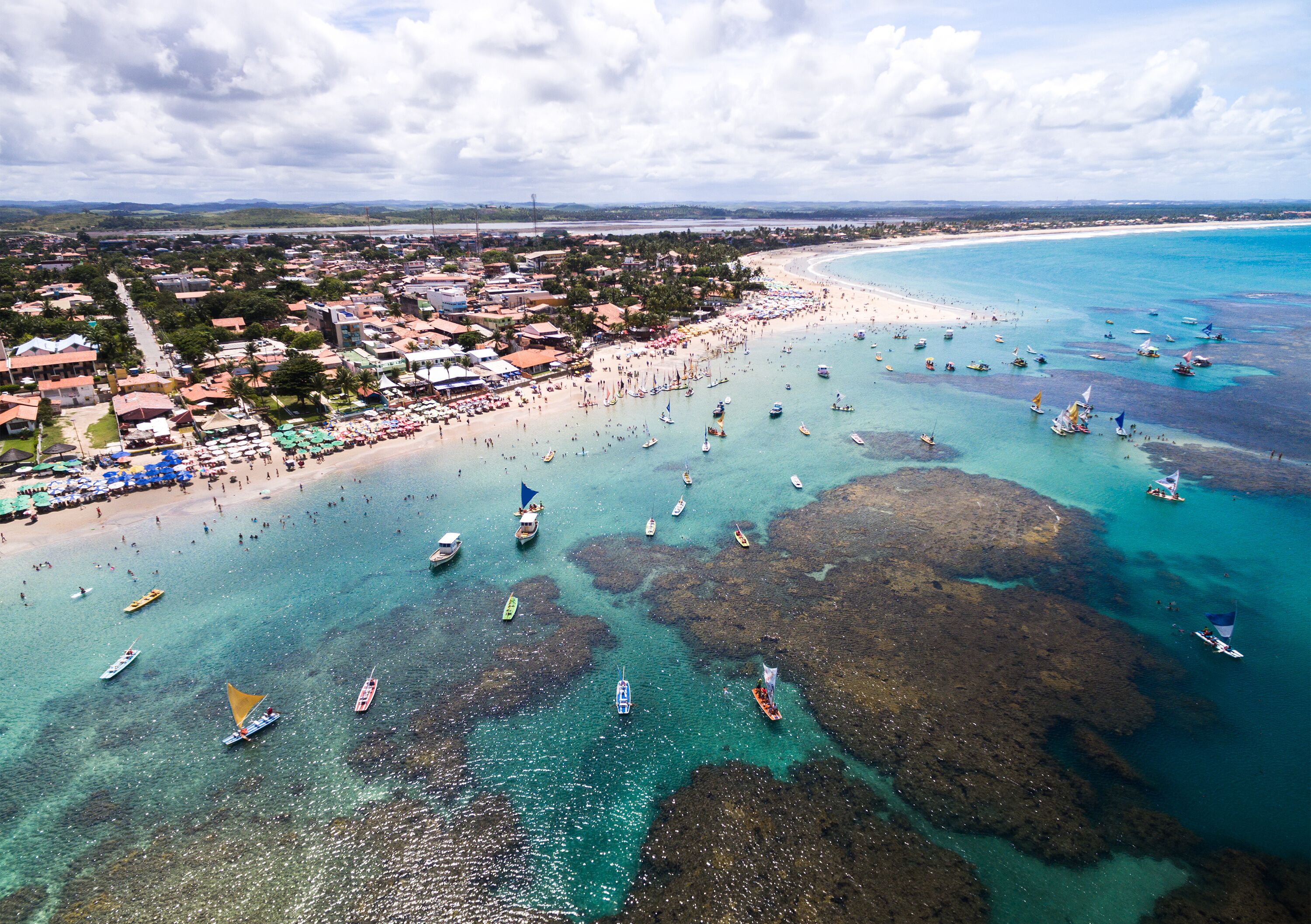 A coastal town with a beach, boats, and clear turquoise waters.