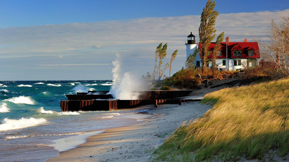 A coastal scene with a lighthouse, a red house, and waves crashing against a wooden barrier.