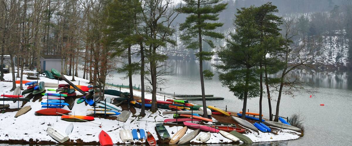 Colorful canoes, kayaks and rowboats, laying in the snow by a lake in the winter