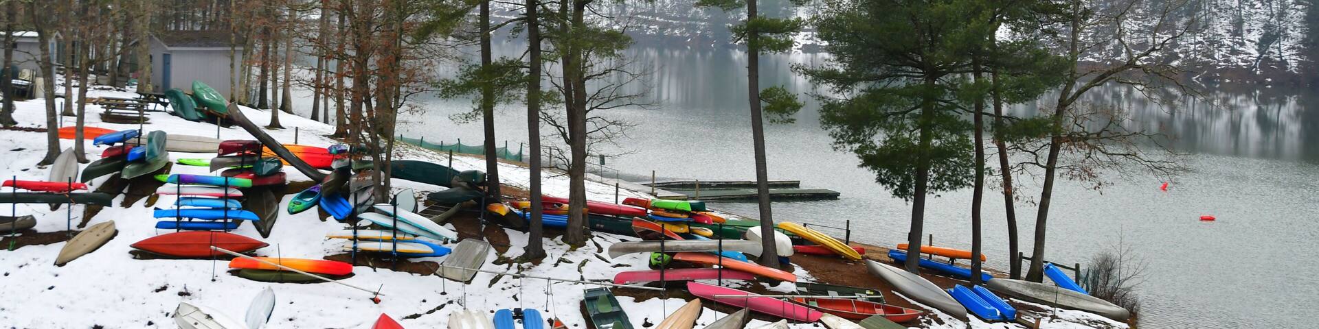 Colorful canoes, kayaks and rowboats, laying in the snow by a lake in the winter