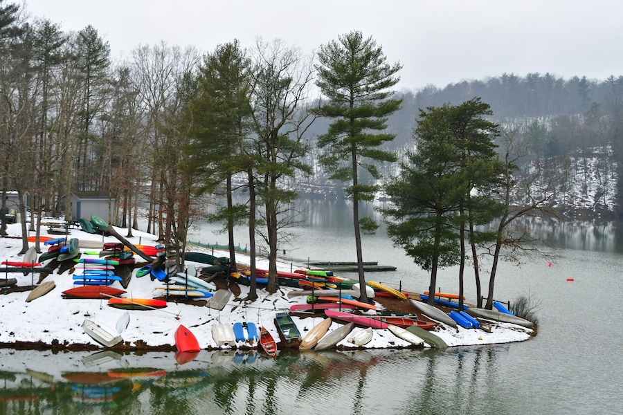 Colorful canoes, kayaks and rowboats, laying in the snow by a lake in the winter