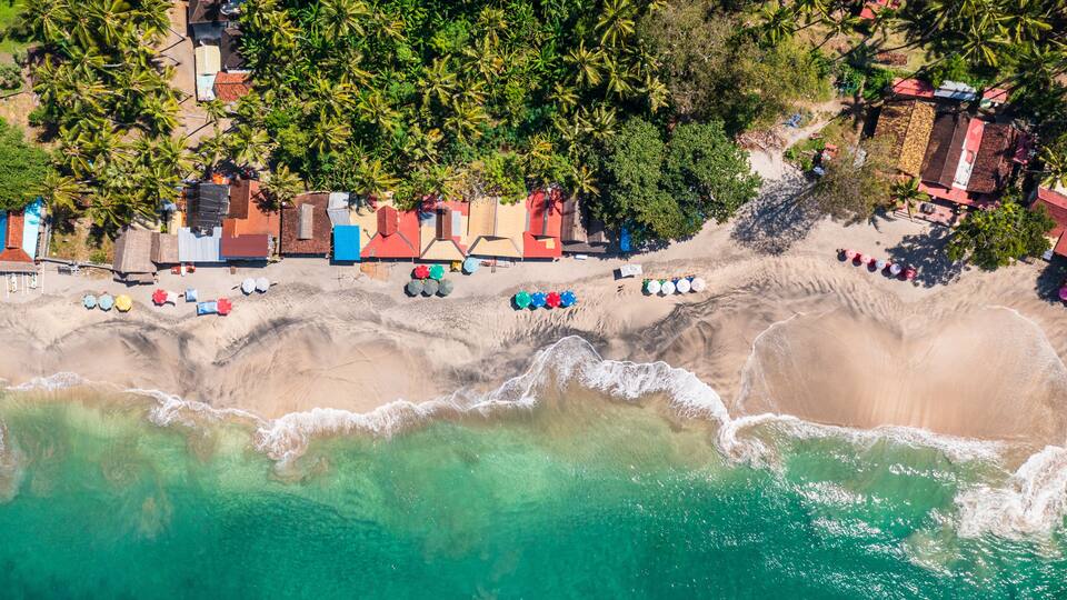 A coastal area with a beach, palm trees, and colorful beach huts.