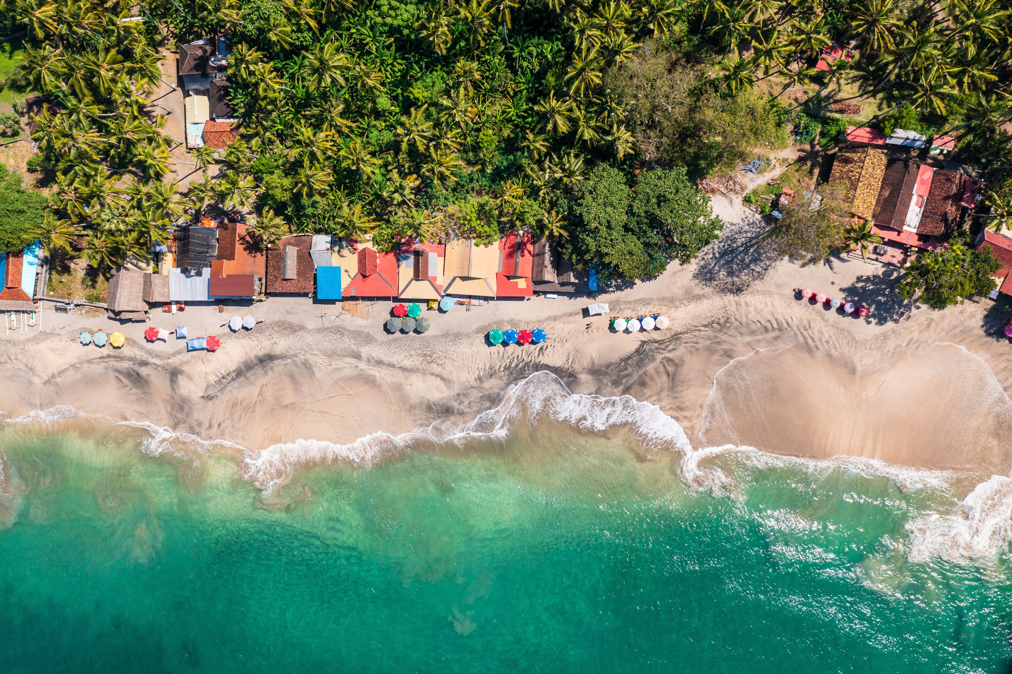 A coastal area with a beach, palm trees, and colorful beach huts.