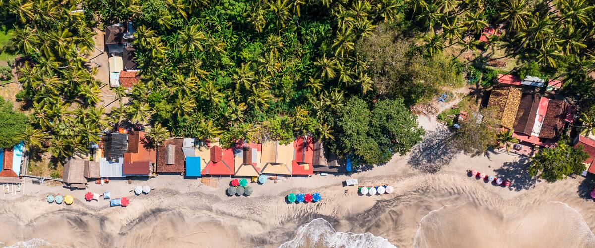 A coastal area with a beach, palm trees, and colorful beach huts.