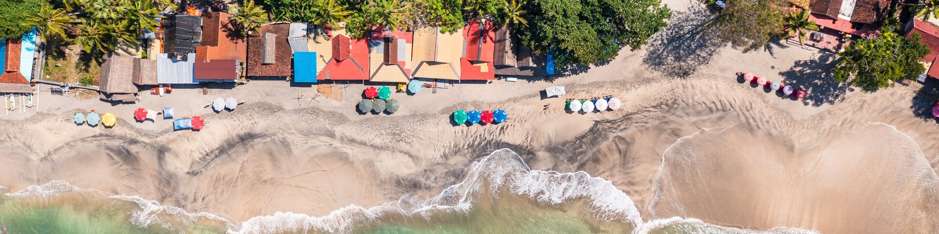 A coastal area with a beach, palm trees, and colorful beach huts.