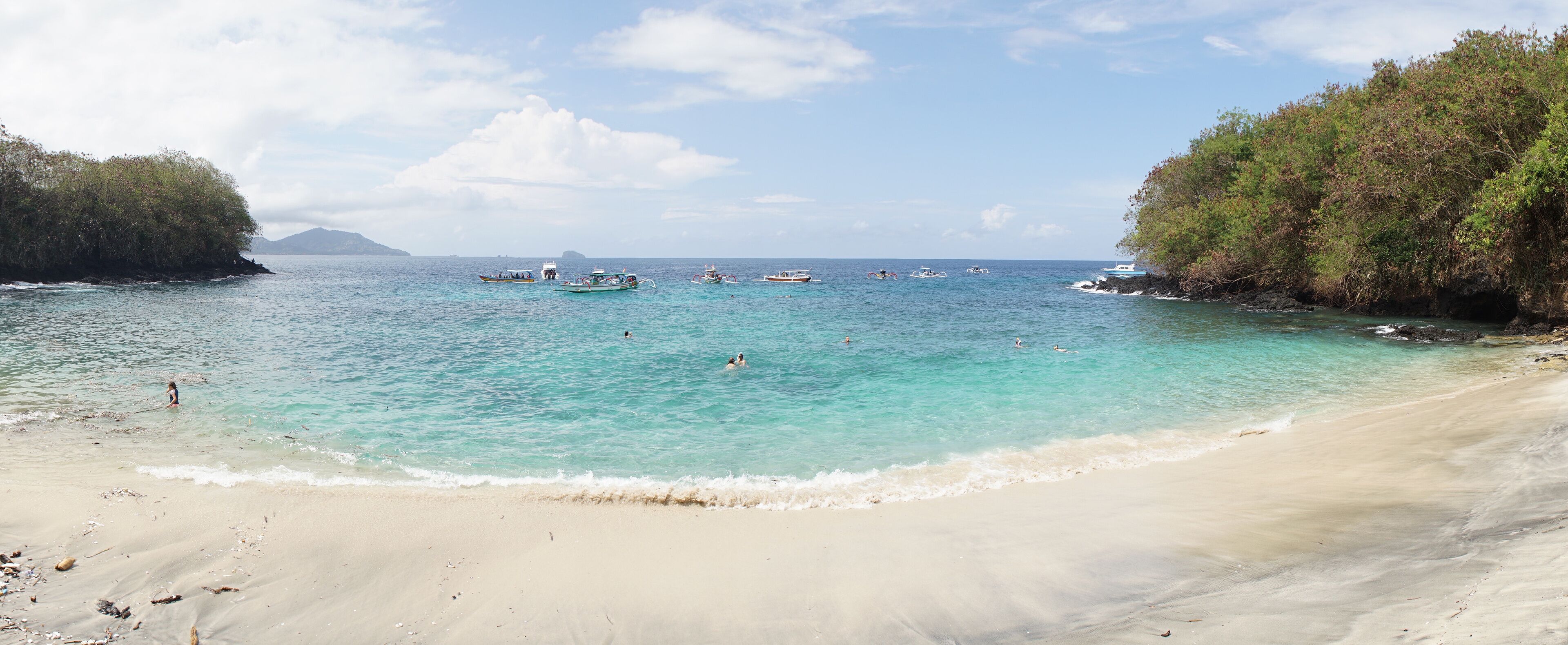 Boats and people visiting Tropical Blue Lagoon Beach near Bali in Indonesia.