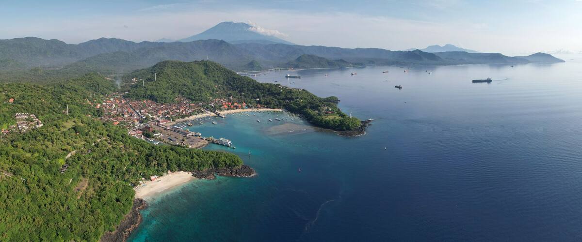 An aerial view of a coastal town with a bay, boats, and a mountainous backdrop.