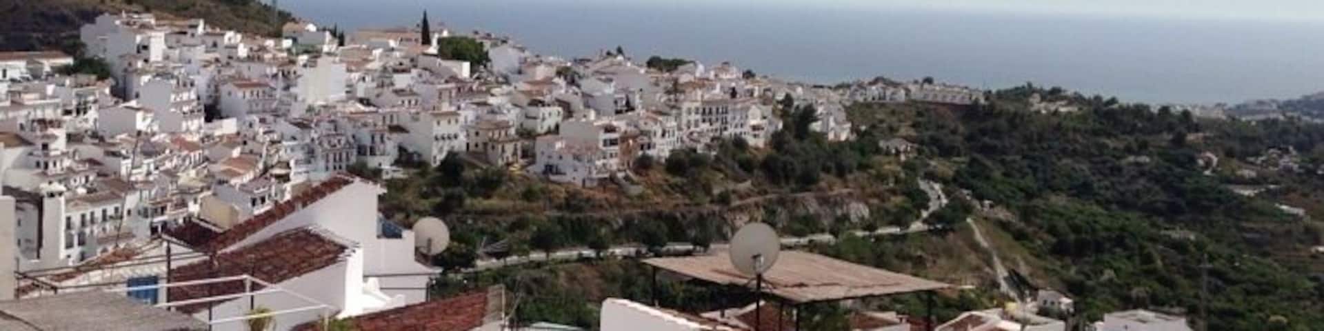 A coastal town with white buildings, terraced roofs, and a view of the sea.