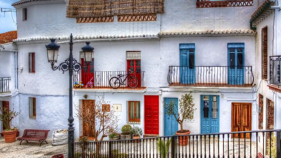 A white building with red and blue doors, a bicycle, and a bench.