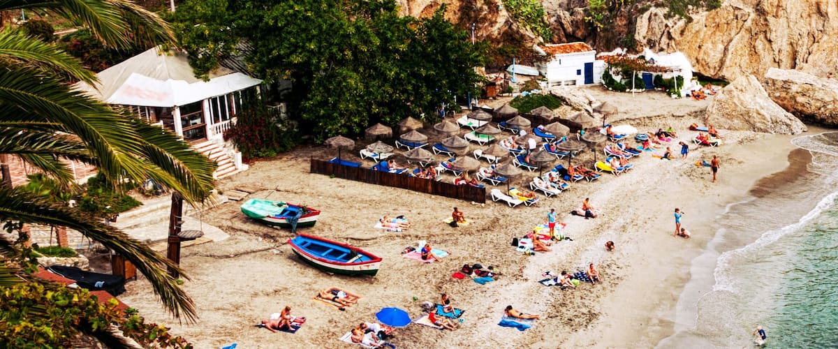 A beach with people sunbathing, umbrellas, and boats.