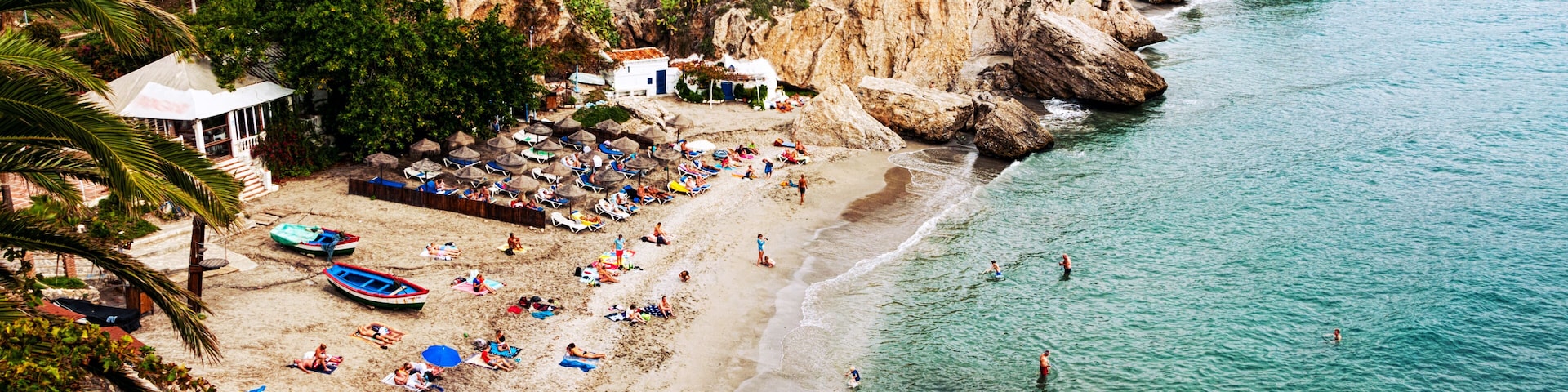 A beach with people sunbathing, umbrellas, and boats.