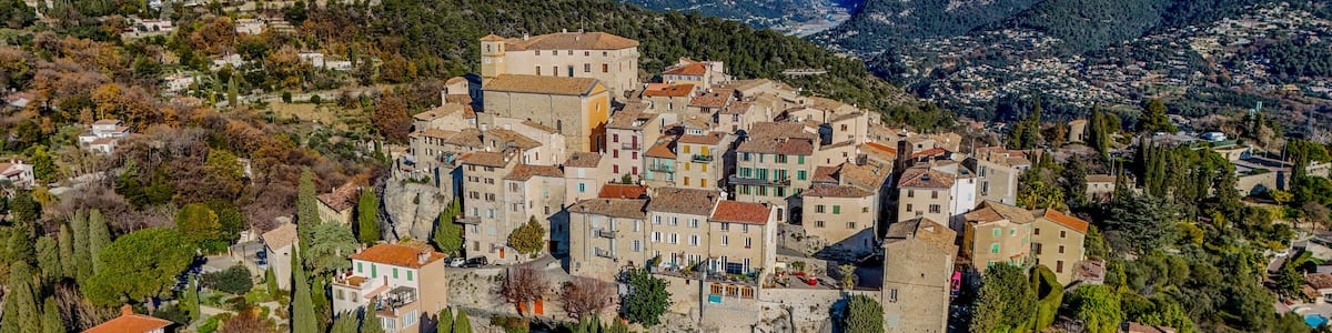 A mountainous village with terraced houses, a winding road, and snow-capped peaks in the background.