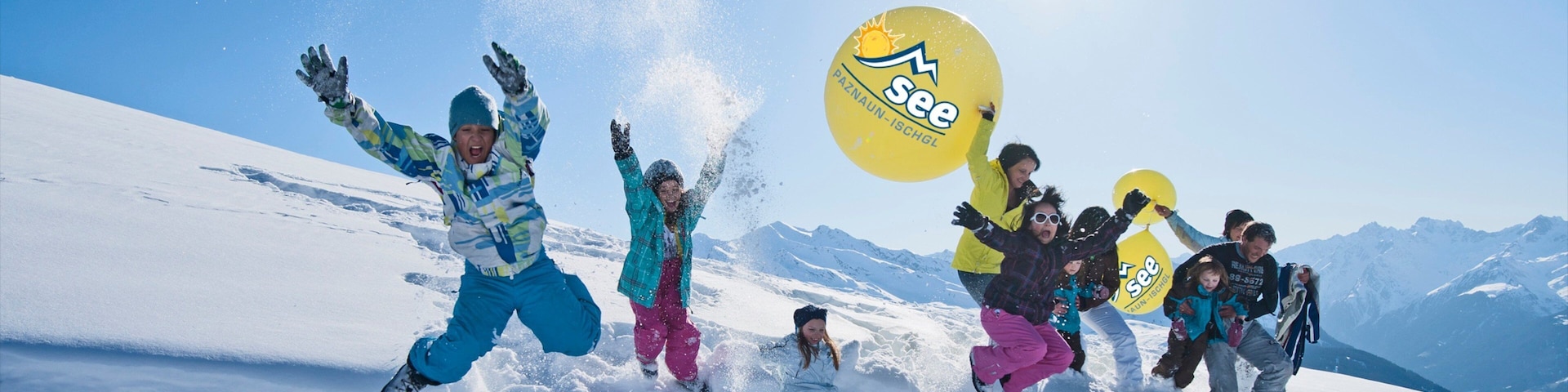 Un grupo de personas haciendo snowboard en una montaña nevada con un cielo azul despejado y picos nevados al fondo.