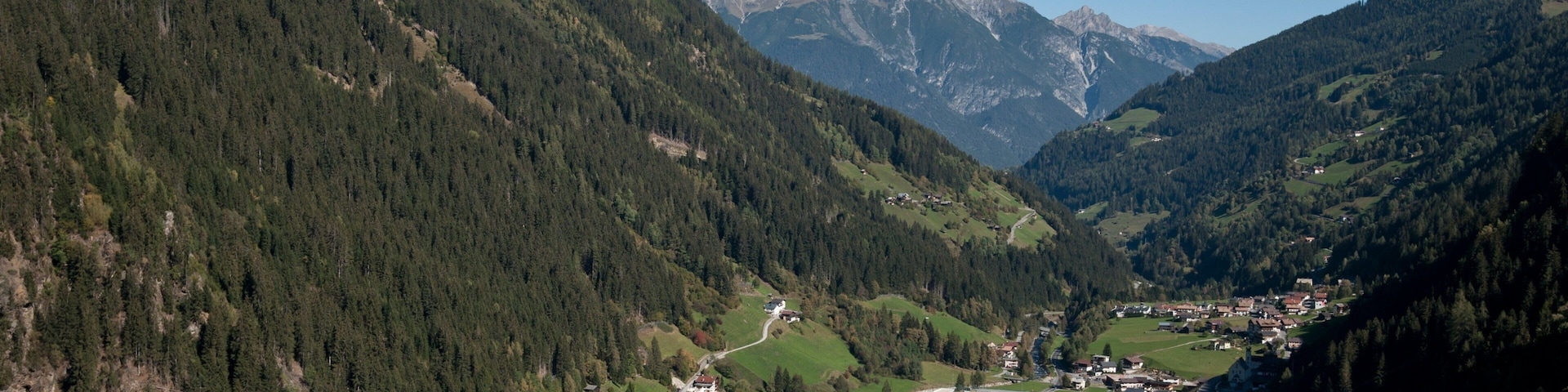A mountainous landscape with a valley town surrounded by forests and snow-capped peaks.
