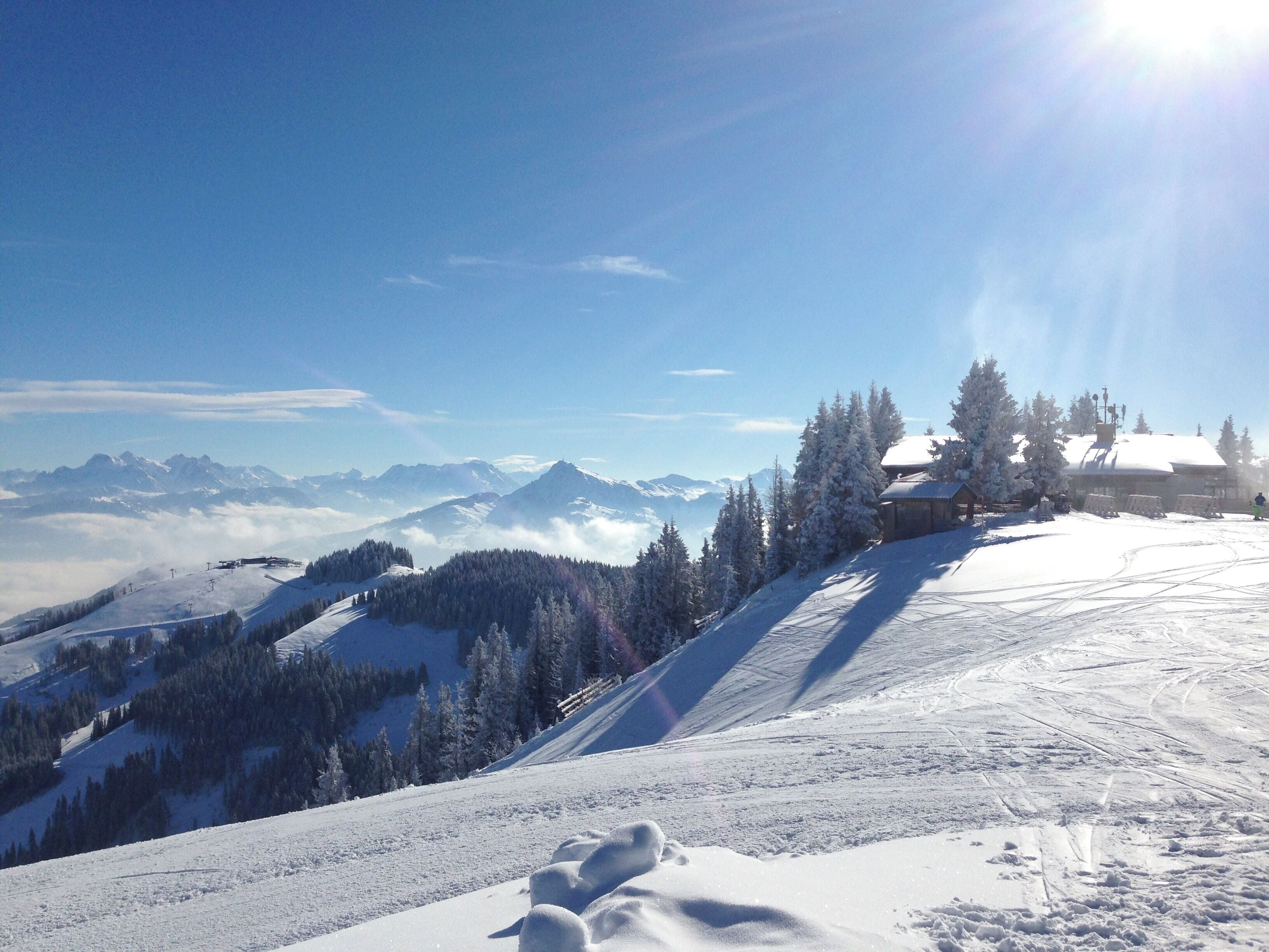 A snowy mountain landscape with a ski resort, snow-covered trees, and distant mountains under a clear sky.